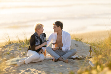 Fototapeta premium Couple enjoying wine on a sandy beach at sunset