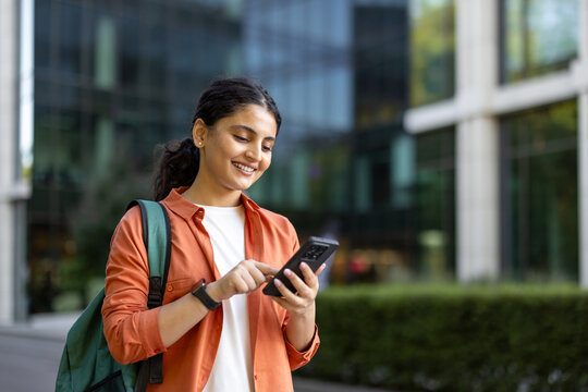 Young indian woman carrying a backpack and interacting with a mobile phone, representing campus life, digital communication, and connectivity for learning and personal use
