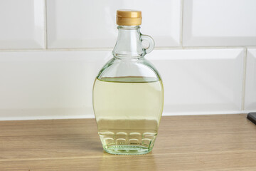 A clear glass bottle filled with vinegar sits on a wooden counter against a tiled wall.