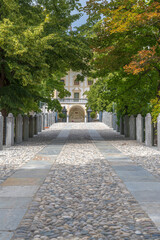 Fototapeta premium The famous castle in the small village of Aymavilles, Aosta Valley, Italy, with the entrance facade. Cobblestone avenue in the foreground. Big trees with green leaves at both sides.