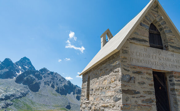Little chapel named "Cappella di San Grato" close to the famous Deffeyes hut, Aosta Valley, Italy. Mountains and blue sky on the background. The inscription on the facade is in Latin.