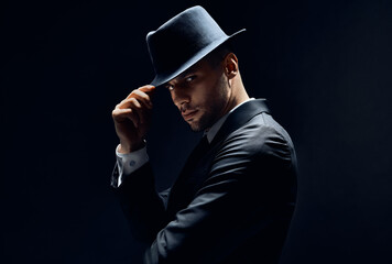 Young handsome man in black suit touch his hat on dark background
