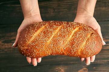 Loaf of fresh made white bread in woman hands on wooden table background