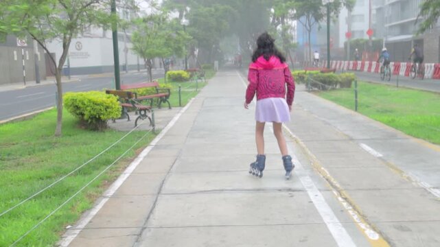Back view of young girl inline skating on urban park path