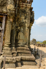 Intricate bas-relief of a standing figure adorns the weathered sandstone wall of Phnom Bakheng temple near Siem Reap, Cambodia. The historic structure features ornate patterns and ancient motifs © Florent