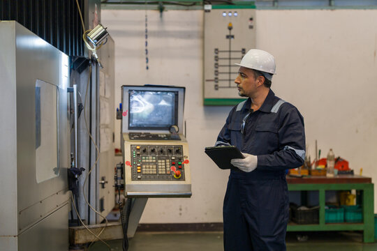 Engineer using digital tablet controlling CNC machine in modern industrial factory workshop. Professional technician monitoring automated manufacturing process industry technology maintenance concept