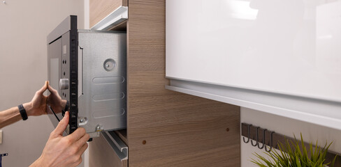 Obraz na płótnie Canvas integrated microwave oven installation in the domestic kitchen. household appliance service. copy space