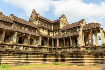 Fototapeta premium Oblique view of a weathered sandstone gallery at Angkor Vat, Cambodia, illuminated by natural daylight. The historic Khmer structure features intricate carvings, balustered windows, and layered