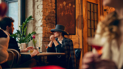 Mature woman in wide brim hat meeting man at cozy cafe table. Concept of business lunch promotion, elegant fashion branding and boutique restaurant advertising visuals.