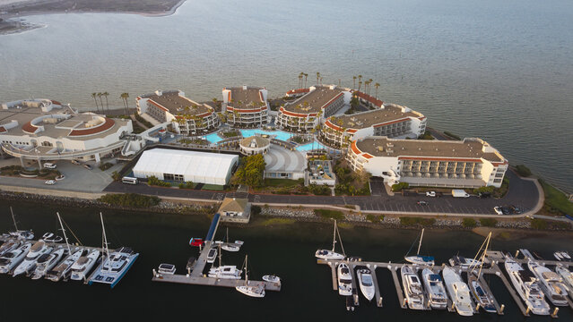 Aerial view of a luxury waterfront hotel with a swimming pool, private beach, and rows of yachts docked at the marina, Coronado, California, United States.
