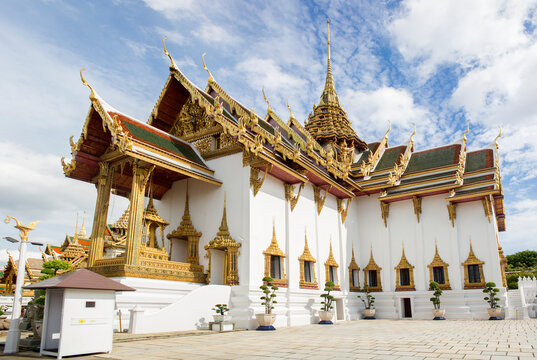 Wide panorama of a grand temple building at the Grand Palace in Bangkok. The structure is characterized by its bright white walls, multiple golden-trimmed windows, and an elaborate multi-tiered roof.