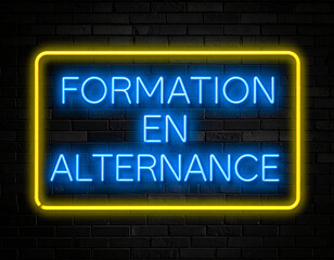 Leuchtende gelbe Neonschrift "Formation en alternance" auf dunkler Backsteinmauer