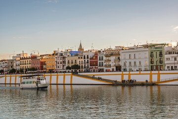 Obraz premium Tourist Boat Passing Colorful Riverside Houses in Triana, Seville