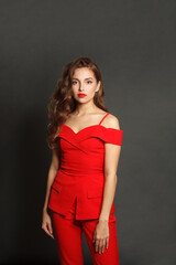 Attractive young woman in red suit standing against black studio wall background