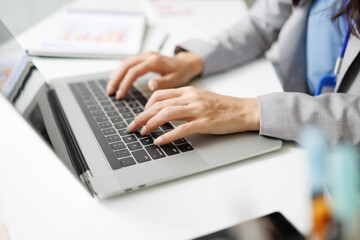 A woman in a gray suit is sitting at a desk with a laptop and a presentation. She is smiling and holding a piece of paper. Concept of professionalism and confidence
