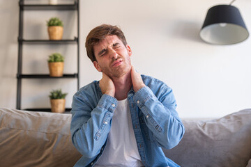 Fototapeta premium Upset tired young man feeling pain massaging stiff neck rubbing tensed muscles to relieve back ache joint shoulder discomfort after long sedentary work in incorrect posture, fibromyalgia concept