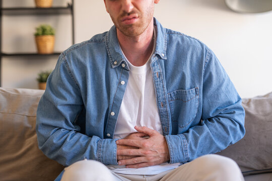 Sick young man in pain holding belly stomach feeling hurt abdomen ache gastritis pancreatitis symptoms or diarrhea, upset adult suffering from indigestion flatulence abdominal problem concept