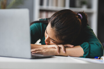 Tired businesswoman sleeping at her desk with a laptop, papers, illustrating workplace fatigue and...