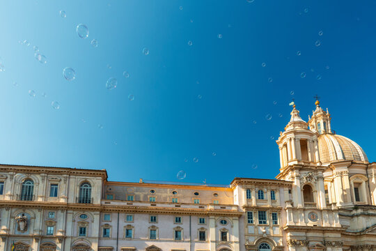 View of Sant Agnese in Agone baroque church with grand dome in Piazza Navona against blue sky with floating soap bubbles, Rome city, Italy. Travel and tourism landmark in Europe