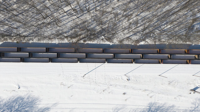 Aerial view of a freight train cutting through a snowy landscape, contrasting the stark white ground with the dark, linear carriages, Framingham, Massachusetts, United States.