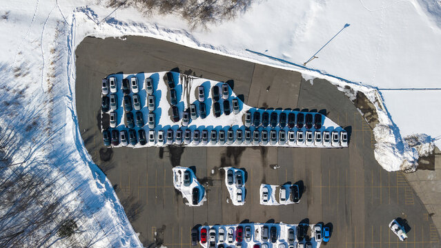 Aerial view of neatly arranged cars casting long shadows on the snowy ground, a stark contrast to the dark trees bordering the lot, Framingham, Massachusetts, United States.