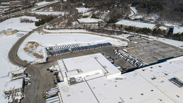 Aerial view of snow-covered roofs and long lines of parked trailers casting shadows on the white landscape, Westborough, Massachusetts, United States.