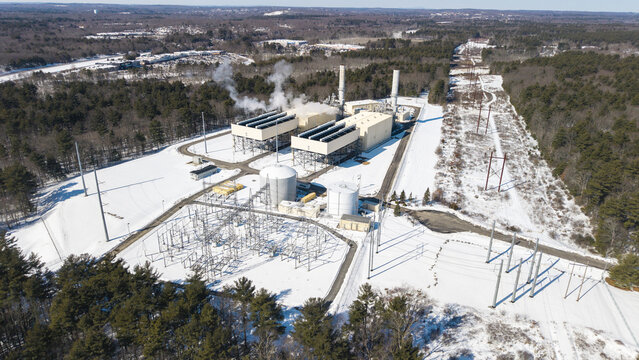 Aerial view of a power plant releasing wisps of smoke into the crisp winter air, surrounded by a blanket of pristine snow, Bellingham, Massachusetts, United States.