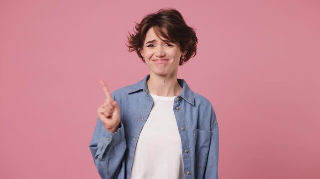 Young woman wears blue shirt white t-shirt casual clothes showing finger gesture no I do not need it point thumb down dislike gesture isolated on plain pastel light pink background. Lifestyle concept