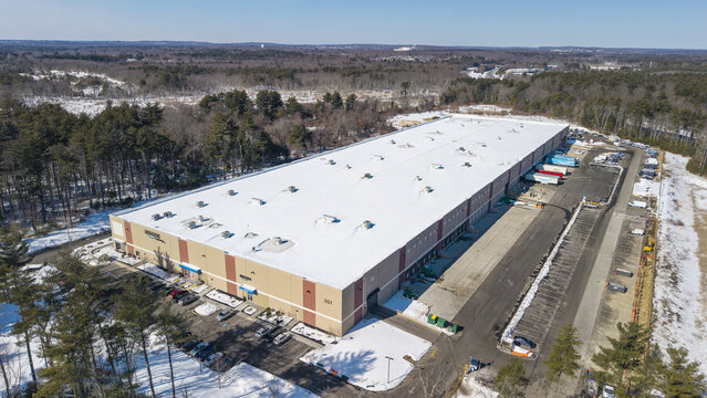 Aerial view of a vast, snow-blanketed warehouse with trucks lined up, contrasting against the stark winter landscape, Bellingham, Massachusetts, United States.