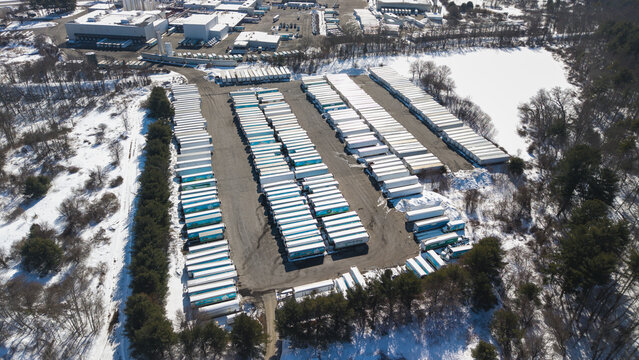 Aerial view of rows of trailers stand stark against the snowy landscape, a metallic grid amidst the winter's embrace, Bellingham, Massachusetts, United States.