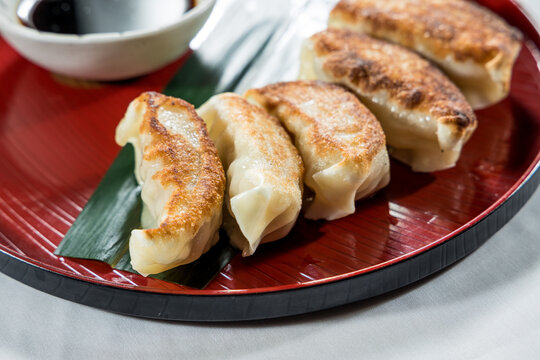 A red plate with golden brown pan-fried dumplings served with soy dipping sauce on the side.