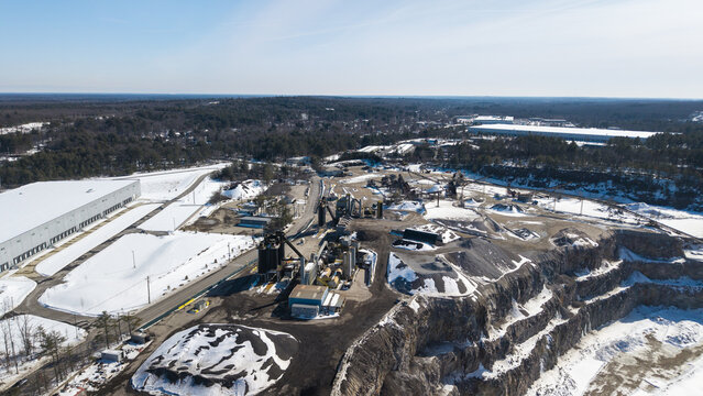 Aerial view of the stark contrast between the industrial quarry's dark textures and the surrounding bright snow-covered landscape, Plainville, Massachusetts, United States.