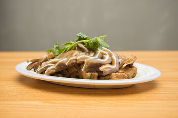 A white oval plate filled with sliced braised offal arranged neatly and topped with fresh herbs.