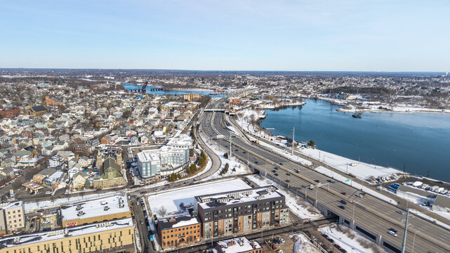 Aerial view of stark white snow blankets rooftops contrasting with the Seekonk River's dark waters as Interstate 195 cuts through, Providence, Rhode Island, United States.