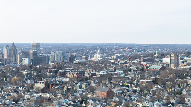 Aerial view of city buildings interspersed with bare trees under a pale sky, a glimpse of the Rhode Island State House, Providence, Rhode Island, United States.