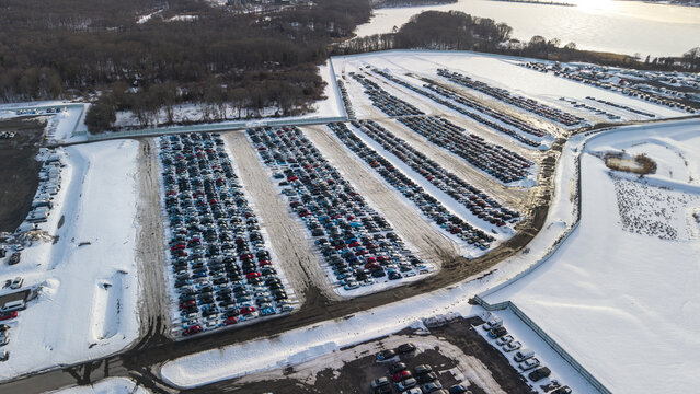 Aerial view of a vast car park covered in snow, contrasting with the dark vehicles and the distant waters, Fall River, Massachusetts, United States.