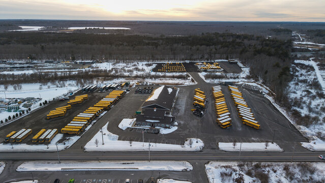Aerial view of rows of bright yellow school buses contrast against the snowy ground near the large building, Bridgewater, Massachusetts, United States.