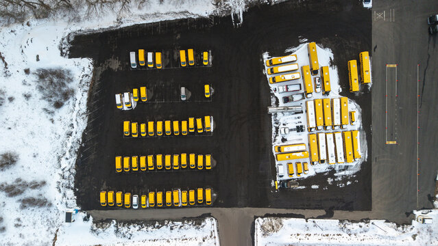 Aerial view of rows of bright yellow school buses parked on dark asphalt surrounded by remnants of winter snow, Bridgewater, Massachusetts, United States.