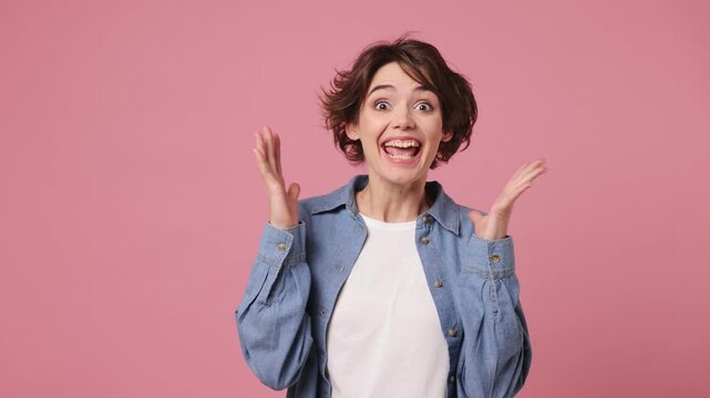 Side profile view surprised young woman she wears blue shirt white t-shirt casual clothes turn around camera cover mouth with hands on face say wow omg no way isolated on plain pastel pink background