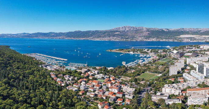 Aerial view of the vibrant coastline of Spinut marina where azure waters meet the lush green Marjan Park forest and the city with Poljud stadium on the right, Split, Dalmatian Coast, Croatia.