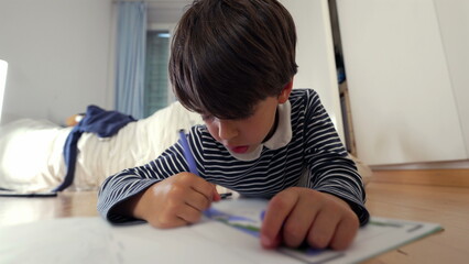 Young boy drawing with a blue marker, sitting on the floor, tongue slightly out in deep concentration, engaged in creative expression, imagination, and learning