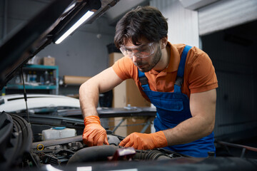 A mechanic checks engine oil with gloves in a garage