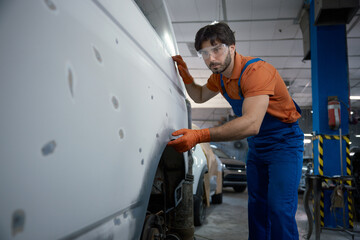 An auto body technician is meticulously inspecting a car panel in the repair shop today