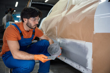 Technician is meticulously prepping a car panel with primer in a garage workshop