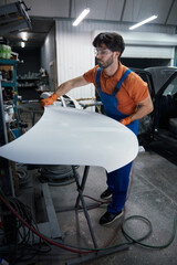 Auto body technician sanding car hood in workshop