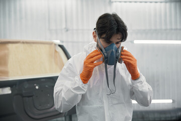 Auto body technician wearing respirator and orange gloves preparing car for paint in workshop