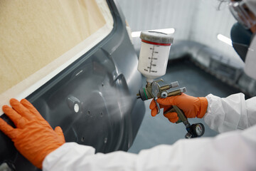 An auto painter dressed in full protective gear is spray-painting a car inside a white garage