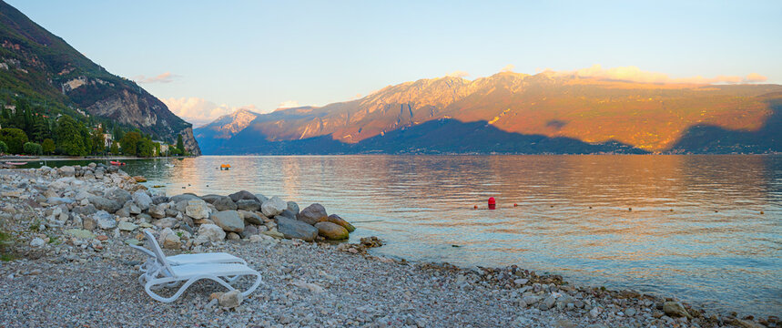 evening scenery gravel beach lake Gardasee, tourist resort Gargnano, last sun over Montebaldo