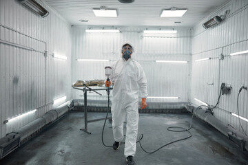 Technician in full protective hazmat suit and respirator inside industrial spray, clean-room booth