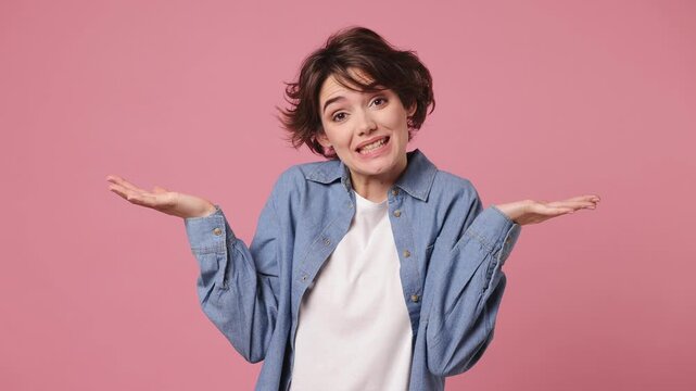 Hesitant sad indecisive young woman she wears blue shirt white t-shirt casual clothes feels doubtful spreading hands say oops ouch oh omg i am so sorry isolated on plain pastel light pink background